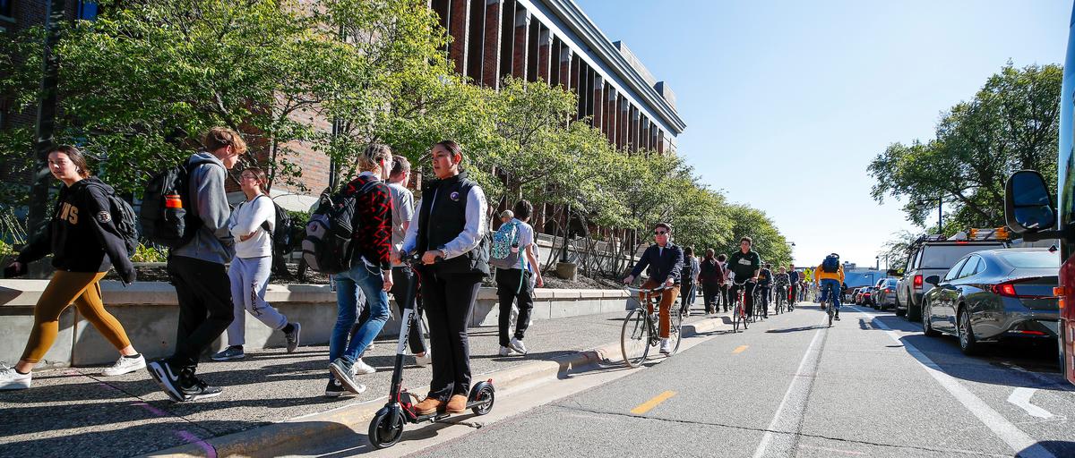 University of Minnesota campus, with cars, a bus, and students walking, biking, and riding an e-scooter.